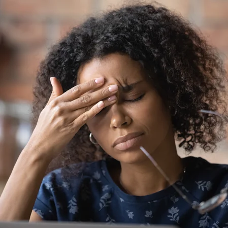 A woman removing her glasses and rubbing her forehead to ease a headache