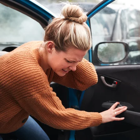 A young woman holding her neck in pain while exiting her vehicle after an auto accident